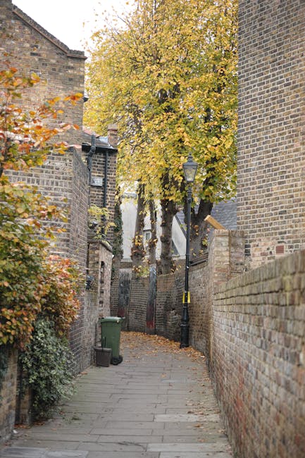 The image shows a historic red brick building with ornate gabled roofs and decorative stone window surrounds, situated behind a brick and stone wall with a black wrought iron fence on top. A white sig